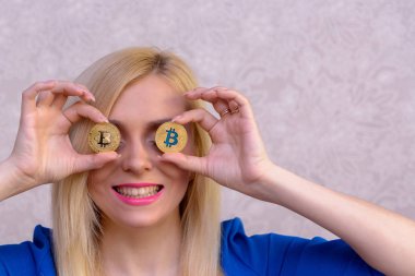 mavi elbiseli güzel bir sarışın kızın elinde iki altın bitcoins