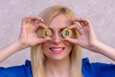 mavi elbiseli güzel bir sarışın kızın elinde iki altın bitcoins