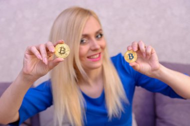 mavi elbiseli güzel bir sarışın kızın elinde iki altın bitcoins