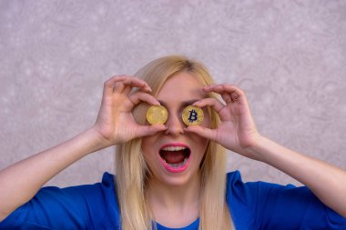 mavi elbiseli güzel bir sarışın kızın elinde iki altın bitcoins