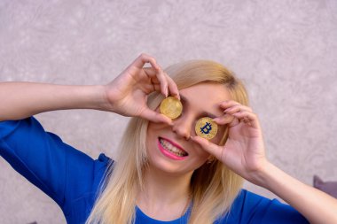 mavi elbiseli güzel bir sarışın kızın elinde iki altın bitcoins