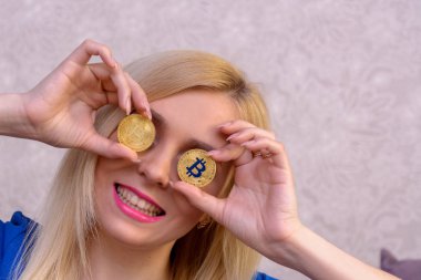mavi elbiseli güzel bir sarışın kızın elinde iki altın bitcoins