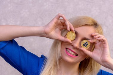 mavi elbiseli güzel bir sarışın kızın elinde iki altın bitcoins