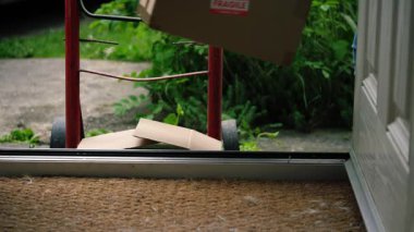 Karton kutular ve yük arabası teslimatı. Evin ön kapısının önünde. 4K seçici odak noktası.