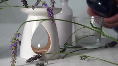 Hand pouring bubble bath with fresh lavender flowers for aromatherapy with oil burner and tea light candle medium zoom shot selective focus
