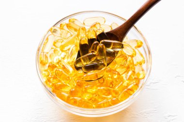 Balık yağı kapsülleri ile bir fincan bir tahta kaşık