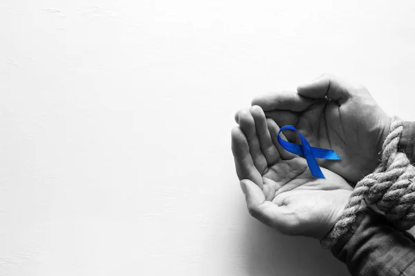 slave with tied hands holds blue ribbon stop slavery, human trafficking and place for text on white background