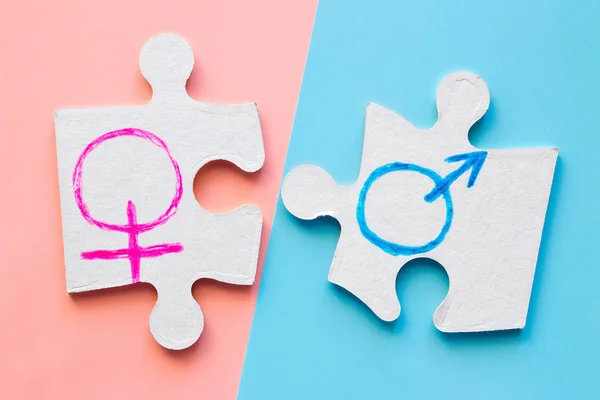 拼图件与男性和女性性别符号上的粉红色和蓝色的背景 概念平等 — 图库照片