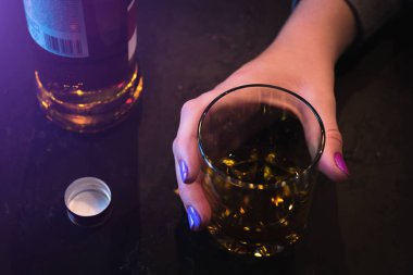 genç bir kadının eli ve siyah bir arka plan üzerinde alkol ile bir bardak