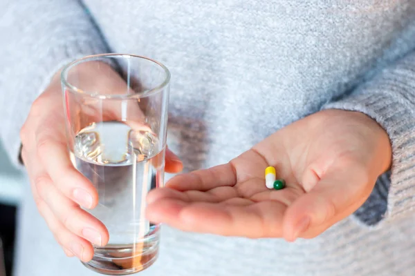 pills in capsules and a glass of water in the hands of a young woman