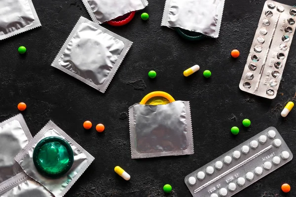 condoms, birth control pills and colored pills on a black background