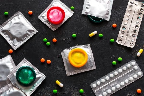 Condoms, birth control pills and colored pills on a black background. Concept of contraception.