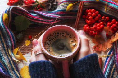 Sonbahar yapraklarının arka planında bir kupa sıcak kahve, bir eşarp ve rowan meyvesi vardı. Merhaba sonbahar konsepti