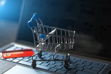 Bir bilgisayar klavyesinde market arabası ve çevrimiçi bir mağazanın arka planında kredi kartı.