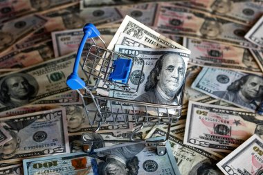 Dolar banknotlarının arka planında para olan market arabası.