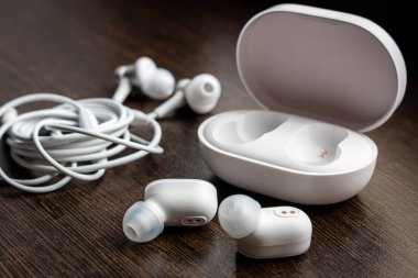 Kablosuz bluetooth kulaklıklar, şarj aleti ve ahşap arka planda birbirine dolanmış kulaklıklar.