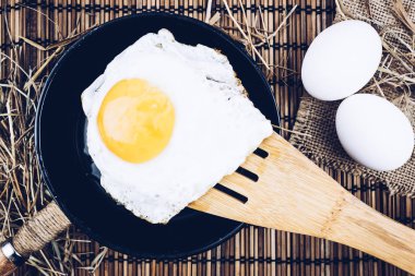 Bir tava üzerinde tahta bir spatula üzerinde sahanda yumurta. Öğle yemeğinde ahşap masa yemek.