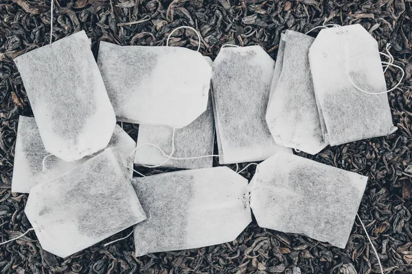 Paper tea bags on dry tea as background