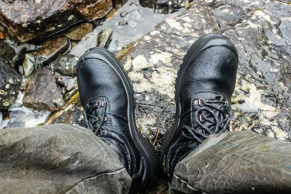 Black mountain boots in river. Footwear for tourist, hiking. Waterproof boots.