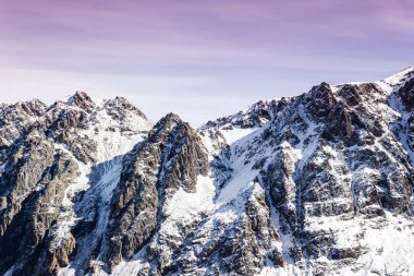 Şafak veya kışın dağlarda günbatımı. Pembe bulutlar altında dağ. Kayalar kar ve mor gökyüzü ile kaplıdır.