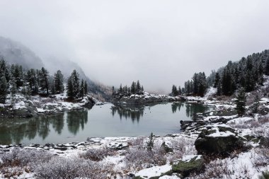 Winter lake, snow in coniferous forest on shore of mountain lake