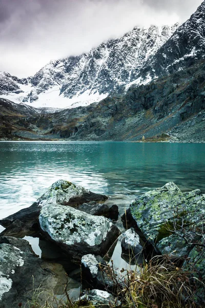 Mountain lake with rocks on horizon. Ridge with snow in valley of turquoise river