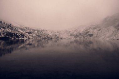 Dağ gölünde mistik sis, suda karlı sırt yansıması