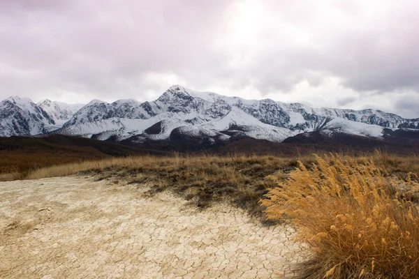 山の谷で乾燥したひび割れた土壌 地平線上の雪山のピーク 草原の秋 — ストック写真