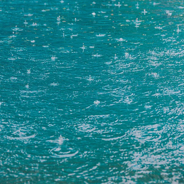 Raindrops on water surface of lake. The turquoise water of river. Rainy weather at sea