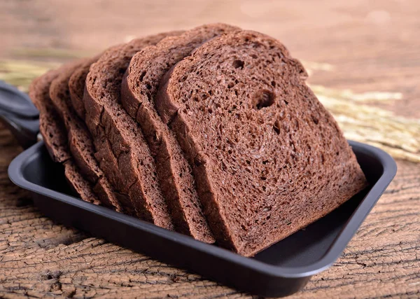 fresh sliced dark cocoa bread in pan on wooden background