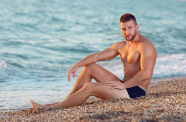 Sahilde oturan seksi fitness model adam