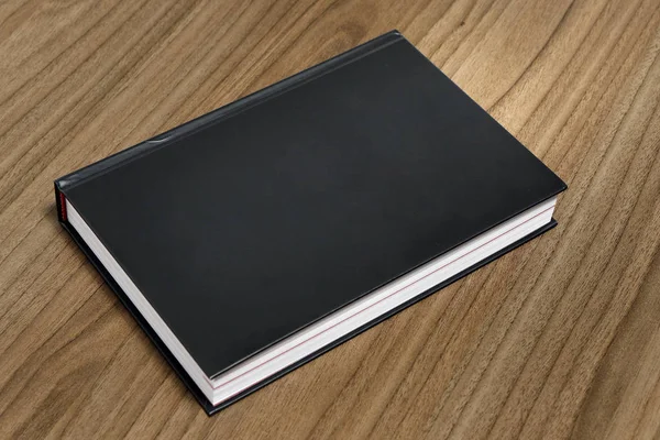 Black hardcover book on flat wood surface - black mock-up book - The book is on the table