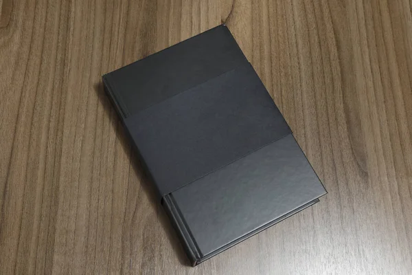 Hardcover black book with cover protector on flat wood surface - black mock-up book - The book is on the table