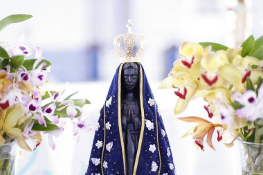 Statue of the image of Our Lady of Aparecida, mother of God in the Catholic religion, patroness of Brazil, decorated with flowers and orchids clipart