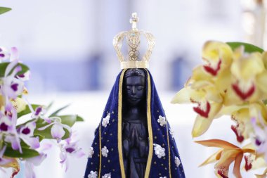 Statue of the image of Our Lady of Aparecida, mother of God in the Catholic religion, patroness of Brazil, decorated with flowers and orchids clipart