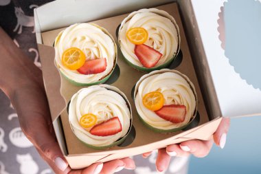 Bir kadın elinde bir demet kek var. Çilek, Kamkat ve krem şanti. Zanaat ambalaj.