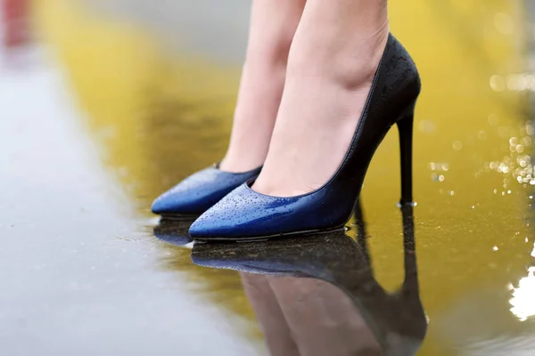 Female feet in shoes on wet asphalt in the rain