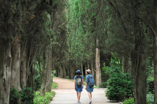 İki genç güzel esmer kız kot elbise ve şapka park uzun yeşil ağaçlar ile yol boyunca yürüyüş.