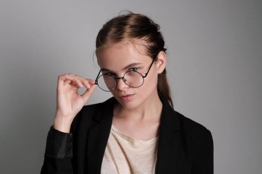 Portre Studio gri arka plan üzerinde siyah ceket kırmızı kahverengi saçlı gözlük güzel genç kızın omuzlarına.