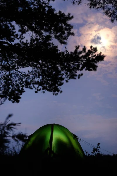 Tente sur la rive de la rivière dans la forêt. Nuit, clair de lune, une lanterne brûle dans la tente. Deux personnes sont assises dans la tente . — Photo