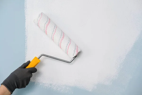 Ręka z rolką farby na ścianie z białą farbą — Zdjęcie stockowe