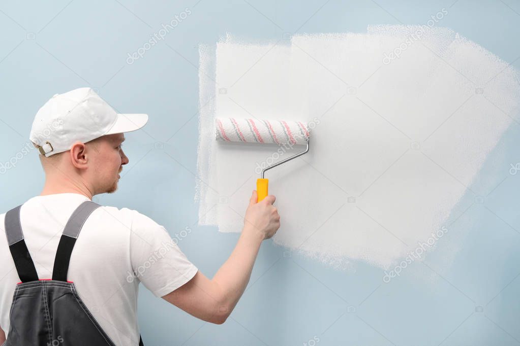 Man working in white T-shirt and cap is painting wall.