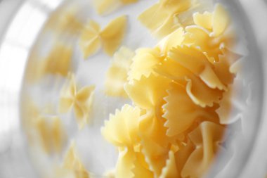 Pişmemiş İtalyan farfalle makarna, beyaz bir arka plan üzerine. Pişmemiş makarna trasparent cam dağınık olduğunu. Unlu Mamüller.