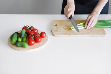 Beyaz bir arka plan üzerinde ahşap bir gemide sebze Dilimleme bir bıçakla eller.