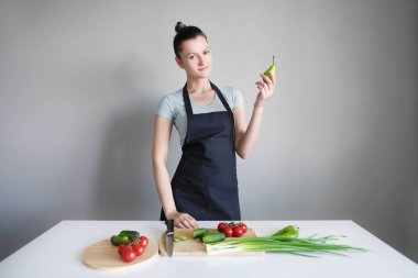 Bir kadın bir mutfak önlüğü içinde yeşil armut gri bir arka plan üzerinde tutar. Beyaz masaya sebzedir.