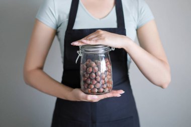 Bir kadın apronda bir cam kavanoz fındık ile mutfakta elinde tutan.