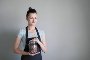 Bir kadın apronda bir cam kavanoz fındık ile mutfakta elinde tutan.