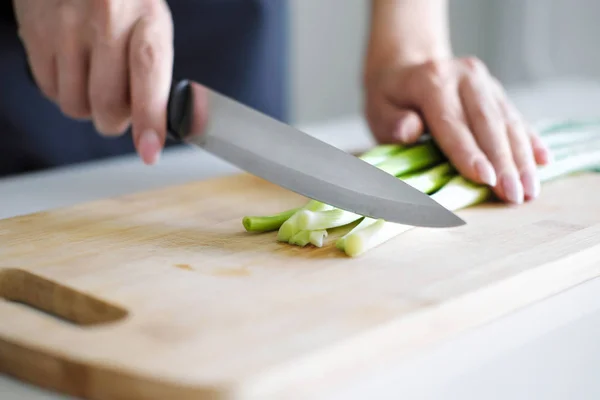 Mani femminili con un coltello, affettare verdure su una tavola di legno su uno sfondo bianco . — Foto Stock