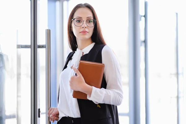 Een mooi meisje in brillen invoert office glasdeur. — Stockfoto