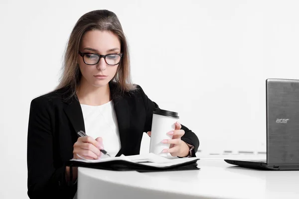 Podnikatel dívka sedí u stolu v kanceláři a práci na notebooku na bílém pozadí. — Stock fotografie